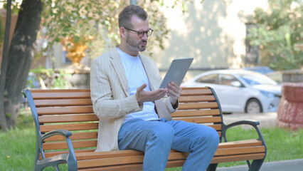 Modern Casual Man Upset by Loss on Tablet while Sitting Outdoor on a Bench