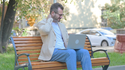 Fototapeta premium Modern Casual Man with Neck Pain Working on Laptop Outdoor