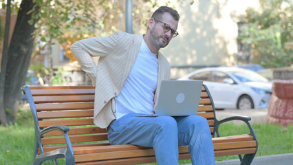 Obraz premium Modern Casual Man Using Laptop with Back Pain while Sitting Outdoor