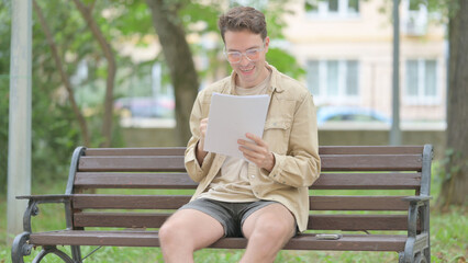 Fototapeta premium Casual Young Man Celebrating while Reading Documents while Sitting Outdoor