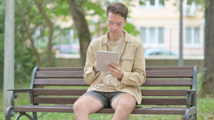 Fototapeta premium Casual Young Man using Tablet while Sitting Outdoor on a Bench
