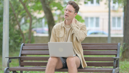 Fototapeta premium Casual Young Man with Neck Pain Working on Laptop Outdoor
