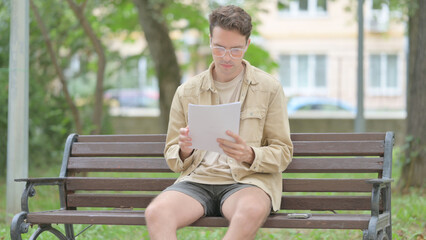 Obraz premium Casual Young Man Reading Documents while Sitting Outdoor