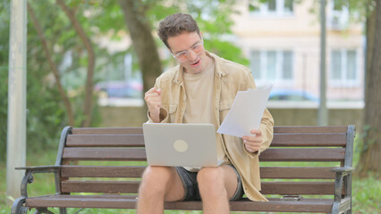 Fototapeta premium Casual Young Man Celebrating while Working on Laptop and Documents Outdoor