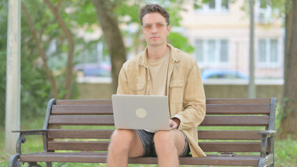 Fototapeta premium Casual Young Man Looking at Camera while Working on Laptop Outdoor