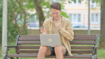 Fototapeta premium Casual Young Man Excited for Successful Online Shopping on Laptop Outdoor