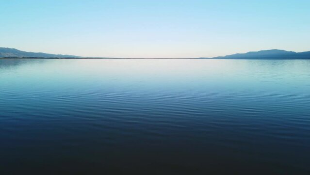 Flying low over a flat lake at sunset with hills on either side. Lake Wairarapa, New Zealand.