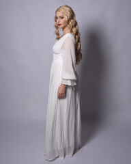 Fototapeta premium Full length portrait of blonde woman wearing white historical bridal gown fantasy costume dress. Standing pose, facing backwards walking away from camera, isolated on studio background.