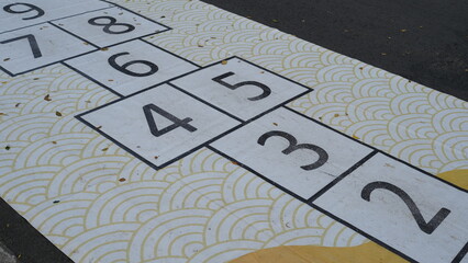 The traditional game involves drawing squares and numbers, by throwing an object into the number...