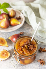 Homemade fig sweet jam in a glass jar with fresh figs on a light gray table. Autumn harvest preservation, healthy fermented food.