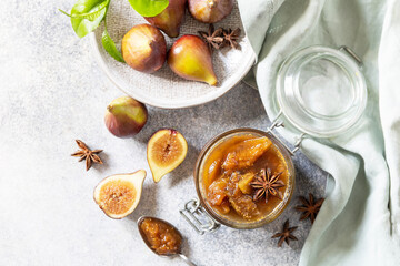 Homemade fig sweet jam in a glass jar with fresh figs on a light gray table. Autumn harvest preservation, healthy fermented food. View from above. Copy space.