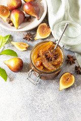 Homemade fig sweet jam in a glass jar with fresh figs on a light gray table. Autumn harvest preservation, healthy fermented food. Copy space.