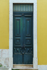 Ornate old high green wooden door of yellow stone building house with white frame decorated with forgings carvings.
