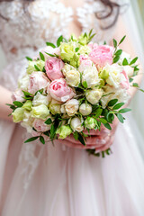 The bride holds a wedding bouquet of roses in her hands
