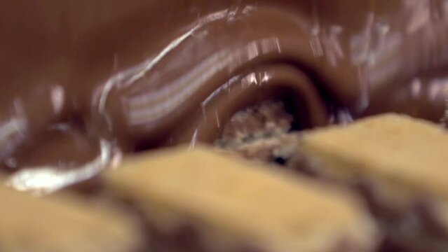 static slow motion macro shot of filled wafer candies being covered with a layer of liquid chocolate