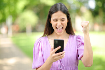Excited woman checking cell phone content outdoor