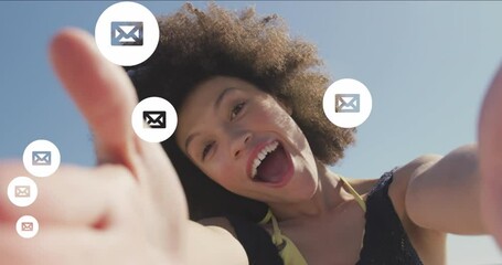 Animation of envelope icons over biracial woman holding camera and blowing kiss at beach - Powered by Adobe
