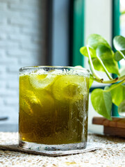 Fresh green tea ice is served in a small glass with a few leaf toppings placed on a placemat, isolated with the surrounding background.