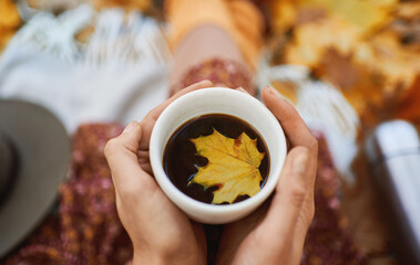 Close up hands holding cup with hot coffee, little maple leafe floating in drinks