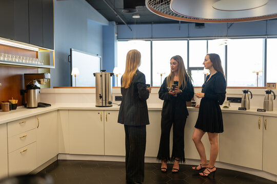 Women share recommendations for interesting books to read in office kitchen during break time. Female employees enjoy coffee break