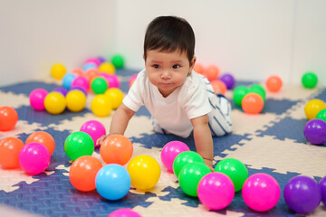 happy infant baby playing colorful balls in playpen