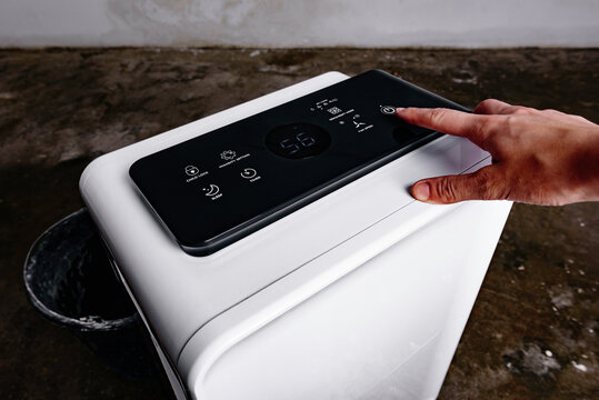 Woman's hand turning on a dehumidifier in the basement to drain the room after water flood.