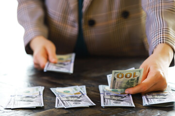 Female hands counting American one hundred dollar bills against the background of smaller bills of...