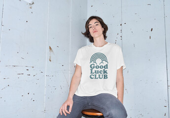 Mockup of woman wearing customizable color t-shirt sitting on stool by wall, flash on camera - obrazy, fototapety, plakaty