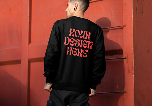 Mockup of man wearing sweatshirt with customizable color by urban building, rear view