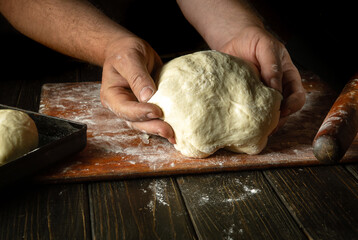 The baker prepares or kneads the dough for baking buns with his hands. The concept of baking confectionery or pies in the bakery