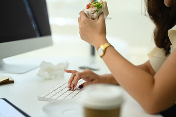 Cropped shot of female office worker sitting at desk and eating sandwich for lunch