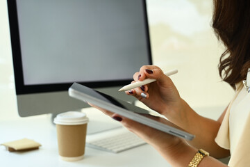Cropped shot of businesswoman sitting at desk and using stylus pen writing on digital tablet
