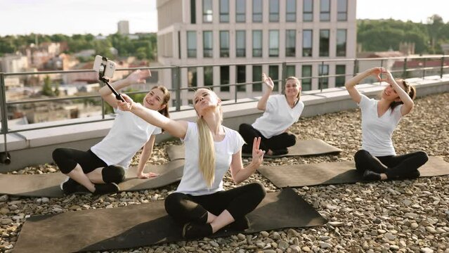 Ladies posing at phone on selfie stick during outdoor yoga