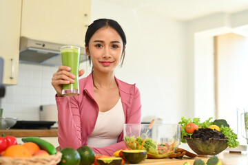 Pretty athletic woman standing in kitchen and drinking healthy juice smoothie. Healthy lifestyle, dieting and loosing weight