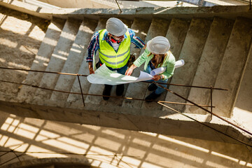 Woman architect and men contractor examining plans on construction site.