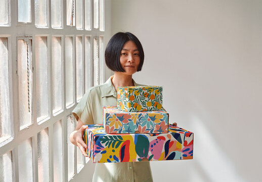 Mockup of Asian woman holding customizable cardboard gift boxes