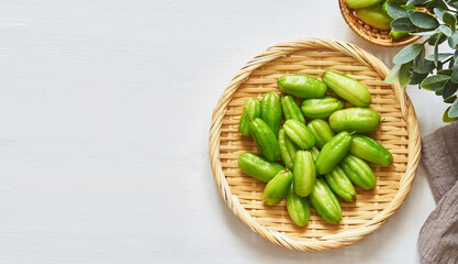 flat lay overhead top view green bilimbi kamias fruit in bamboo plate on white wood table background. green bilimbi kamias on white background. green bilimbi kamias white food table light mood      