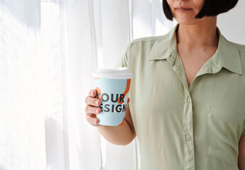 Mockup of woman holding customizable takeaway paper cup with lid