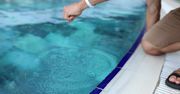 Unrecognizable man puts hand into pool and measures temperature. Comfortable temperature for swimming