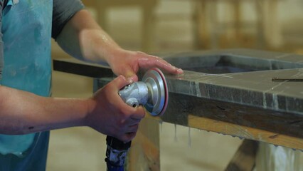 worker polishing edge of granite kitchen countertop - quartz -rock with a polisher with water in a warehouse. United States
