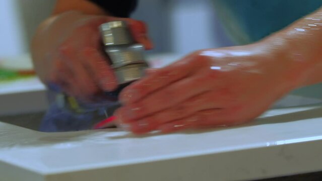 close up of worker polishing edge of granite kitchen countertop - quartz -rock with a blue polisher with water in a warehouse. United States