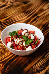salad with cherry tomato, mozzarella balls, green basil leaves, pour balsamic sauce on a wooden table. Italian salad, selective focus.