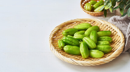 green bilimbi kamias fruit in bamboo plate on white wood table background. green bilimbi kamias in wood plate on white background. green bilimbi kamias on white food table background light mood