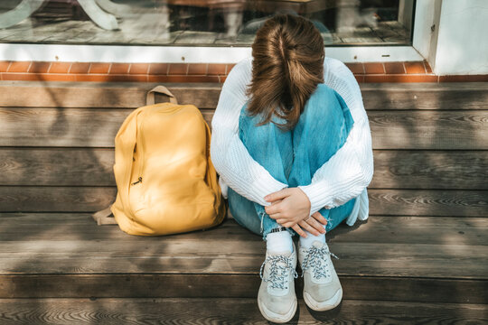 Teenage schoolgirl sitting on a bench hiding her face in her knees, autumn depression, difficulties at school