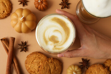 Obraz na płótnie Canvas Pumpkin coffee, female hand, spices, cookies and candles on beige background, top view