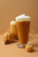 Pumpkin coffee in glasses and candles on beige background