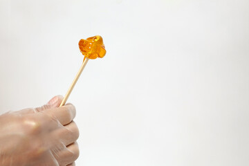 Lollypaste, shugar paste on stick in hand. Shugaring procedure in beauty salon.