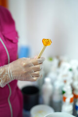 Lollypaste, shugar paste on stick in hand. Shugaring procedure in beauty salon.