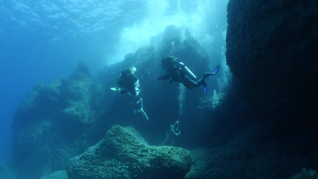  scuba divers exploring underwater topography big rocks