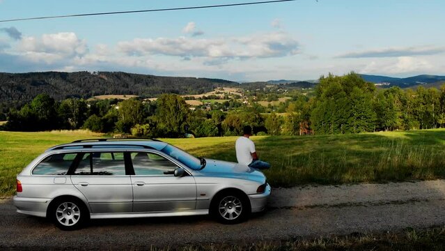 A young man sits in a car and admires the mountain landscape in the Czech Republic. View from a drone of Vratislavice, Liberec urban district in the Czech Republic. A drone view of a village